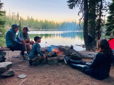 Family sitting around the campfire by the lake. Kid roasting marshmallows