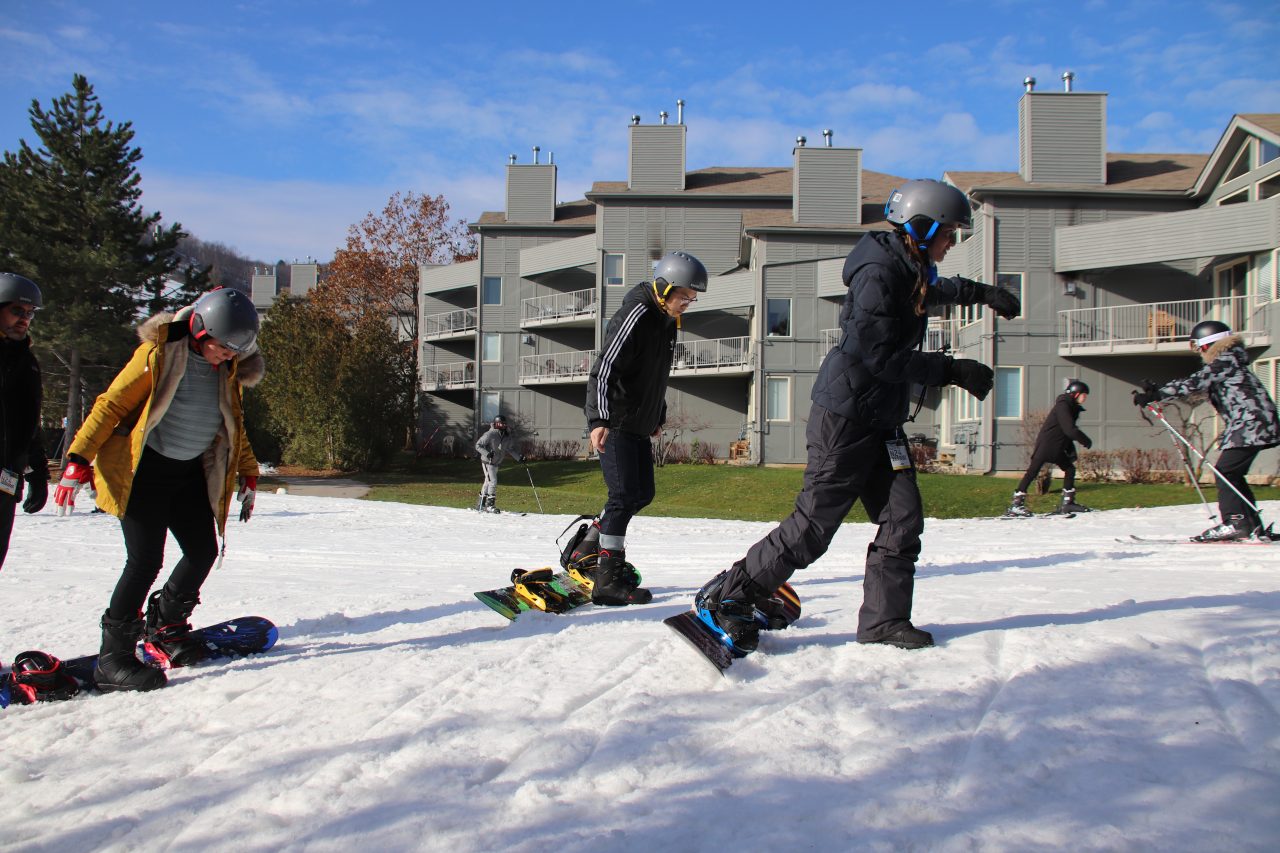 Group of snowboarders learning snowboarding going up the hill with one leg attached to snowboard in Blue Mountain